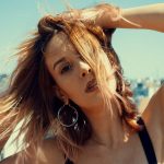 Close-up portrait of a young woman with wind-swept hair on an urban rooftop.