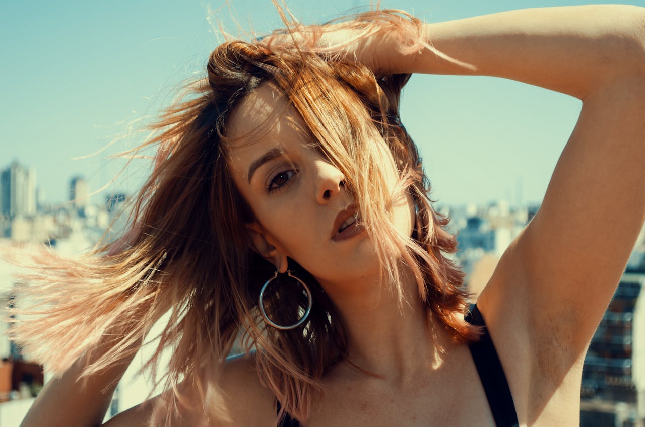 Close-up portrait of a young woman with wind-swept hair on an urban rooftop.